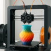 A modern dual extruder 3D printer on a sleek desk setup, printing a detailed multi-color model with spools of filament in the background.